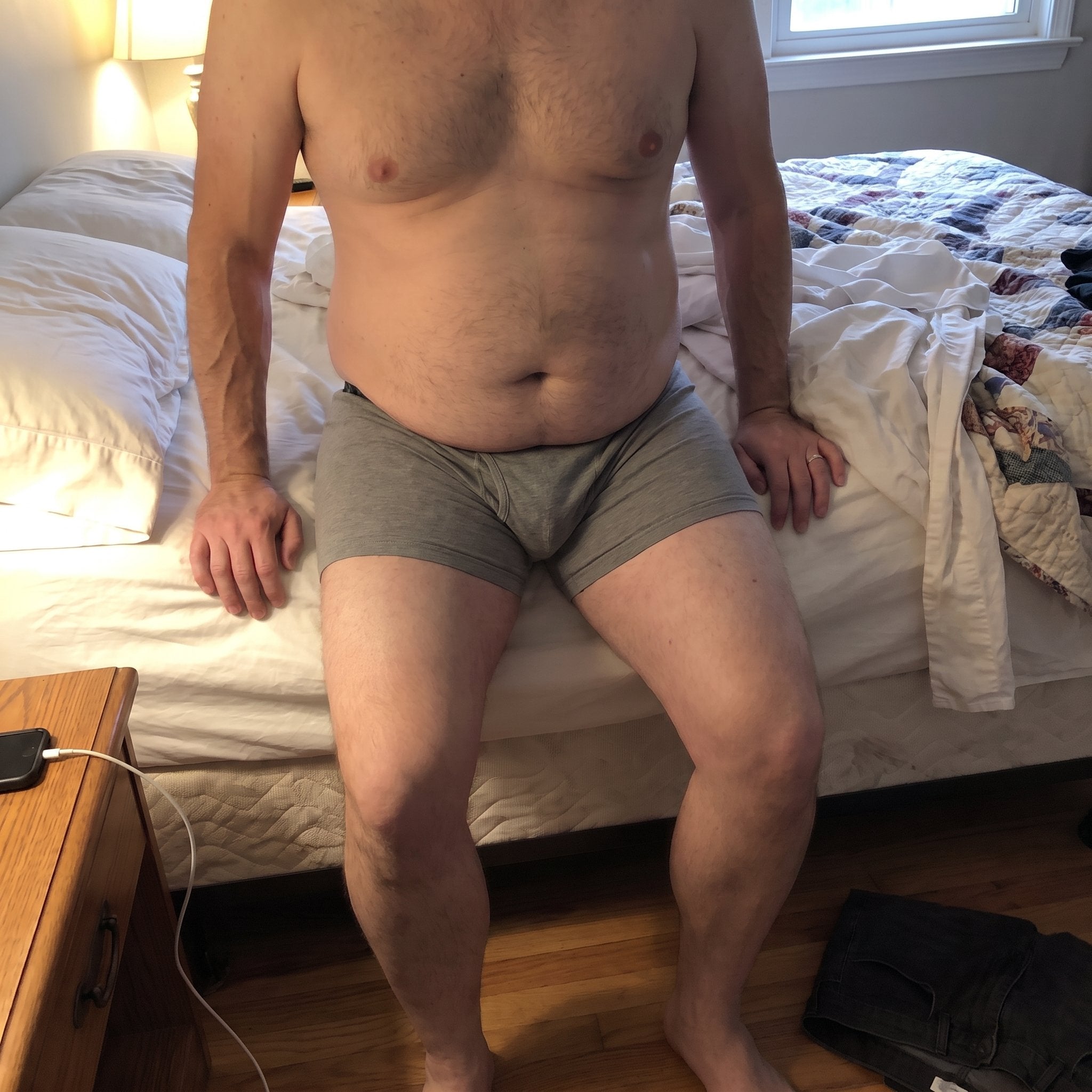 Lean man with a prominent belly sitting on the edge of a bed
